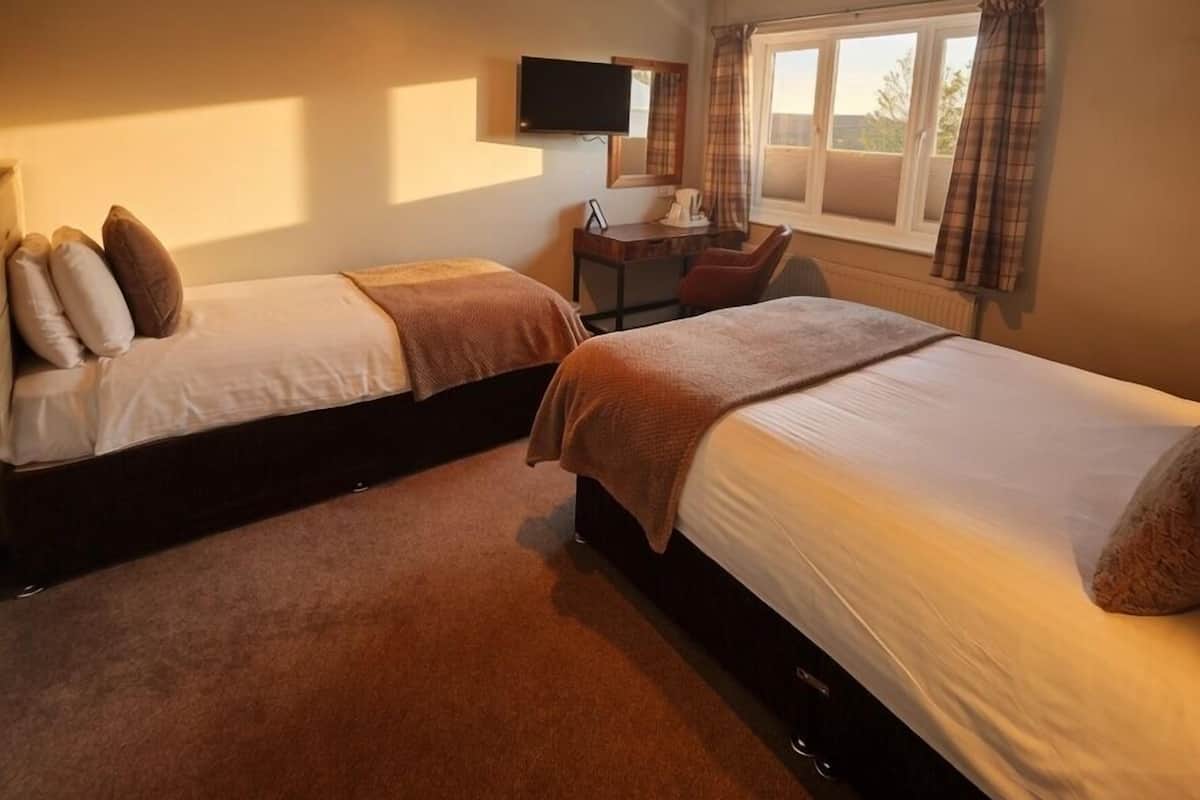 Una habitación de hotel con dos camas, televisión, escritorio y ventana con cortinas.