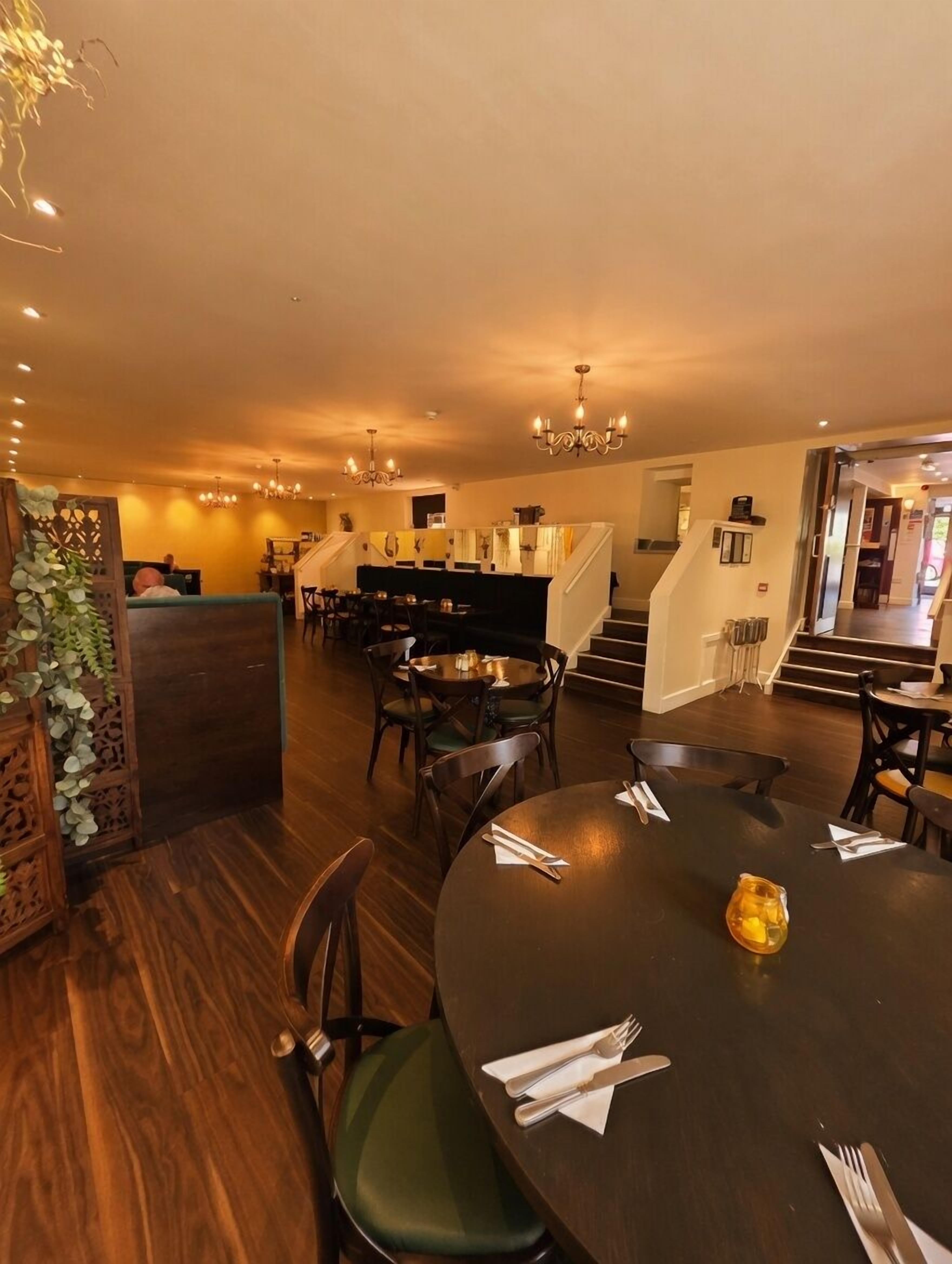 A restaurant with wooden flooring, round tables, and chairs. There are chandeliers hanging from the ceiling.