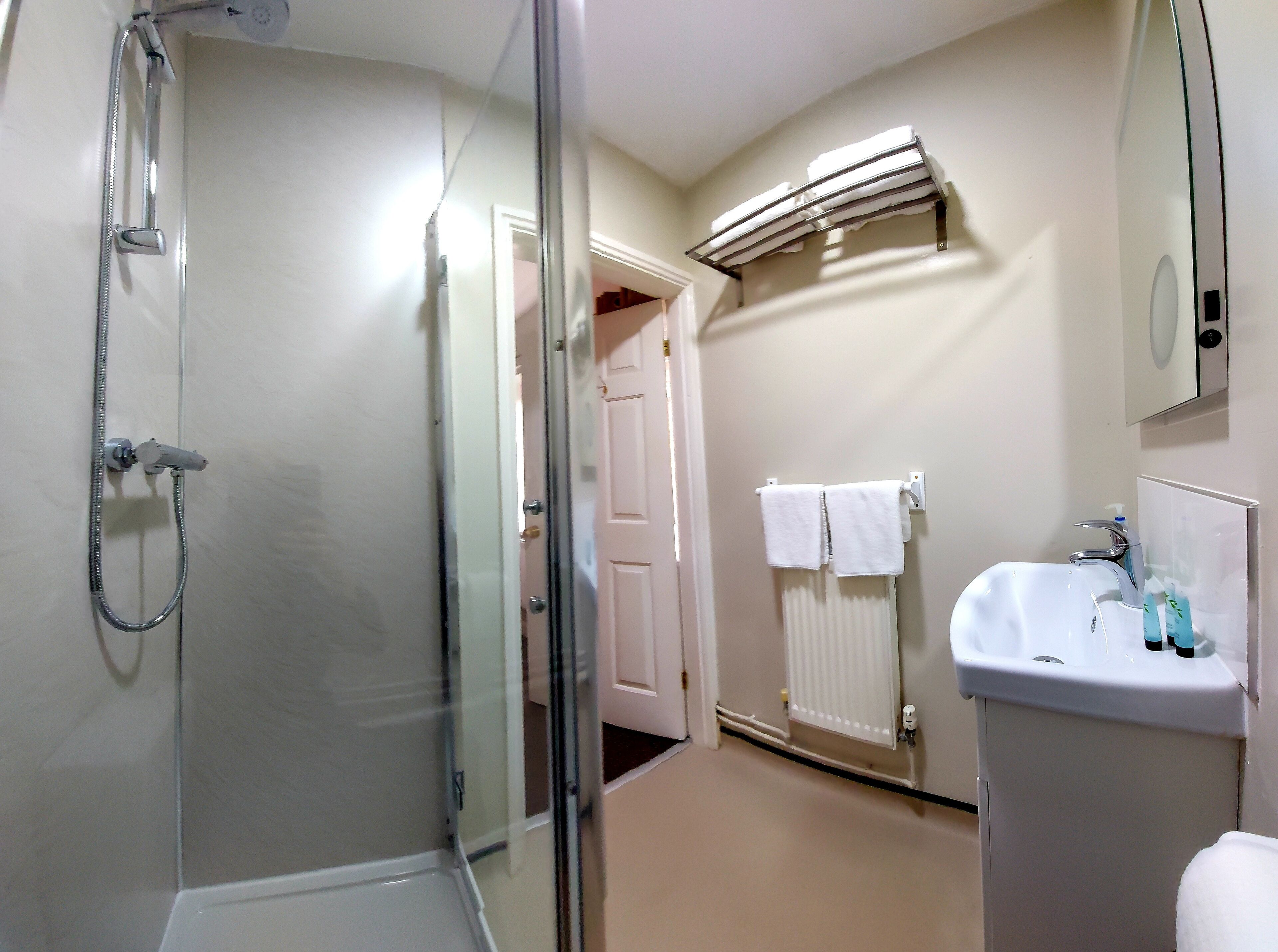 Un baño con ducha de vidrio, un lavabo blanco con espejo y un perchero para toallas.