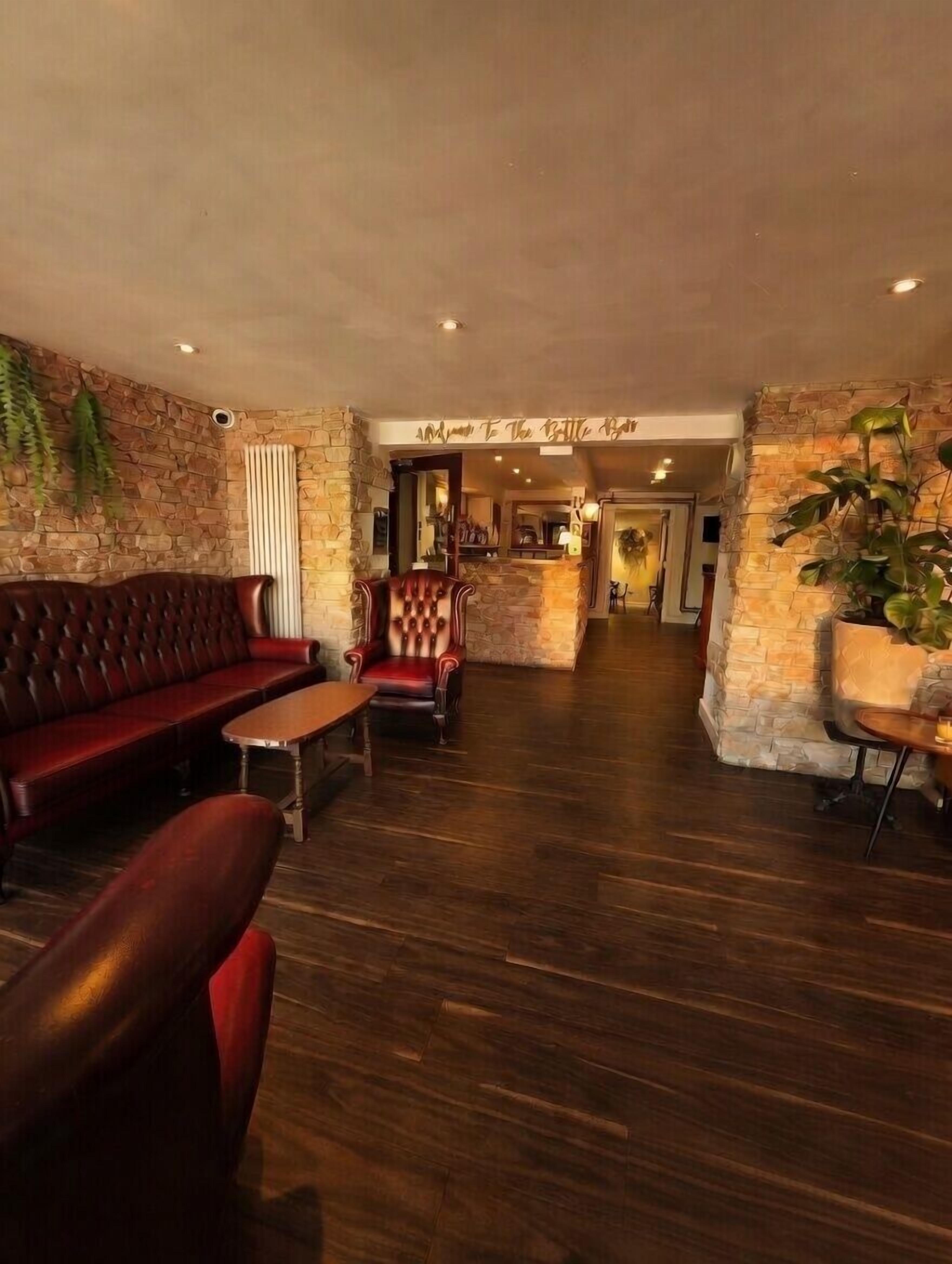 A lobby with a stone wall, a red leather sofa, a wooden coffee table, and a red armchair.