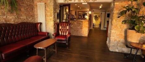A lobby with a stone wall, a red leather sofa, a wooden coffee table, and a red armchair.