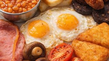 A plate of breakfast food including eggs, sausages, beans, toast, ham, mushrooms, and tomatoes.