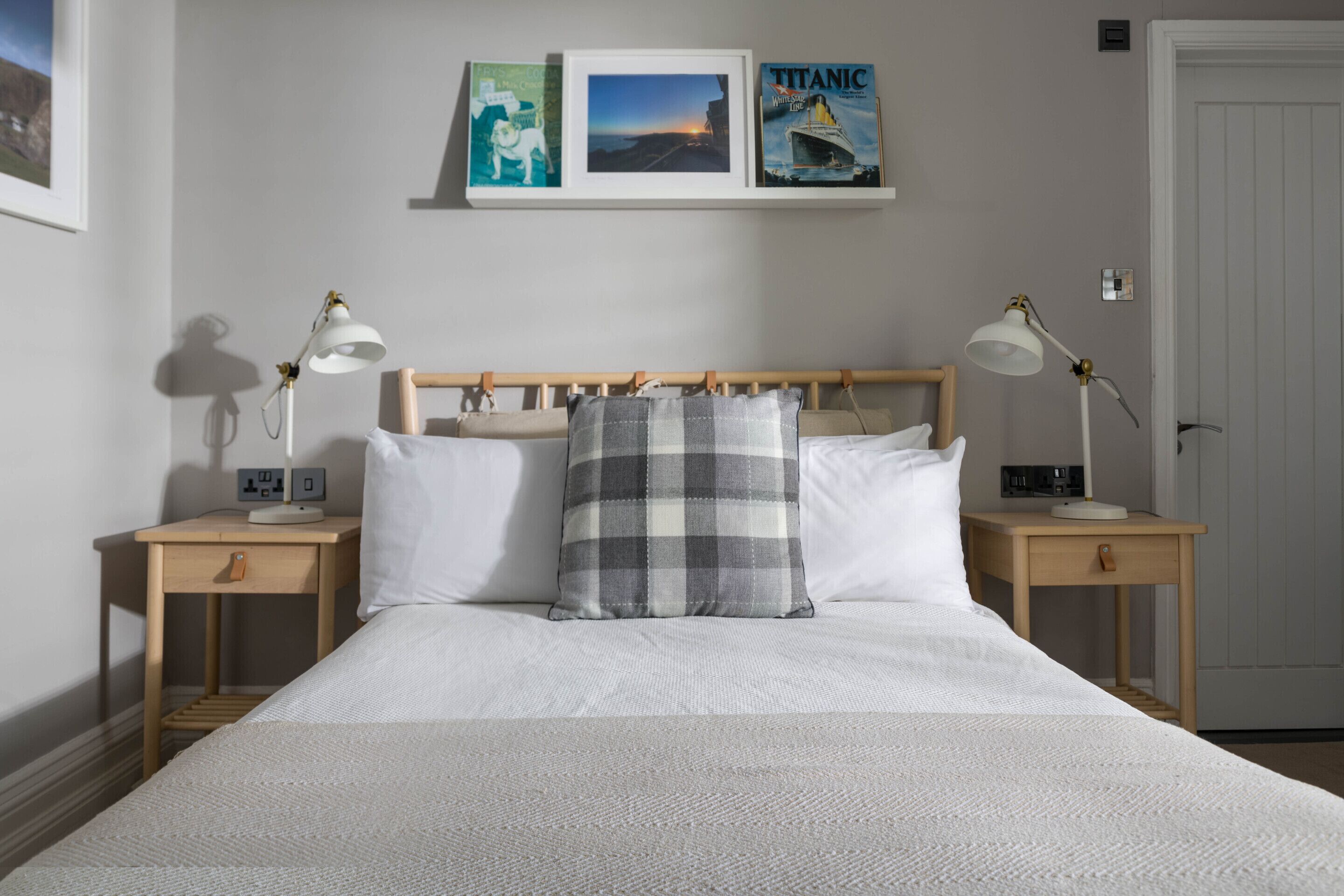 Un dormitorio ordenado con una cama grande, dos mesitas de noche con lámparas, un cabecero de madera y cuadros enmarcados en la pared.