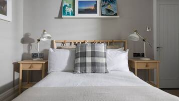 Un dormitorio ordenado con una cama grande, dos mesitas de noche con lámparas, un cabecero de madera y cuadros enmarcados en la pared.