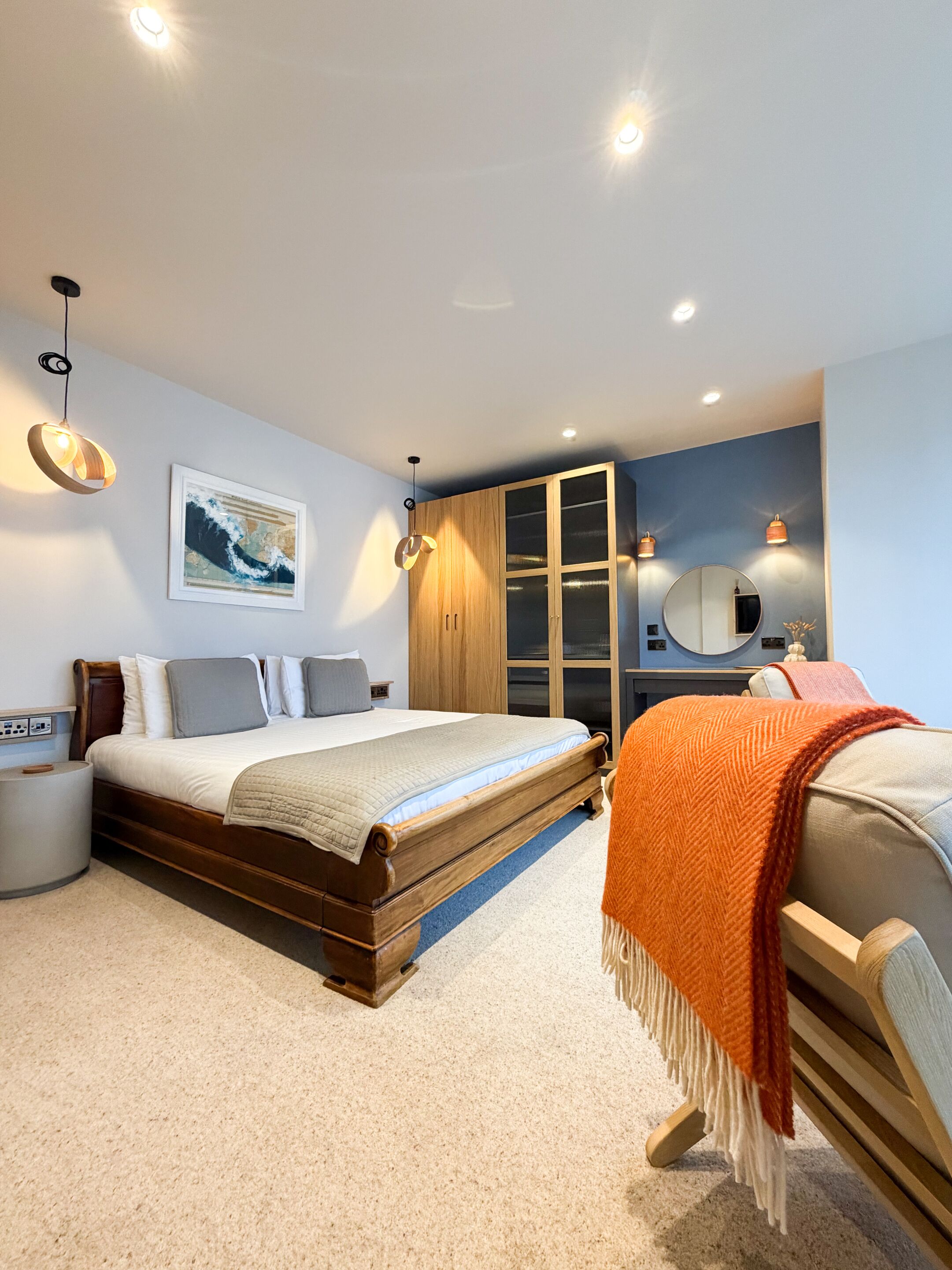 Un dormitorio moderno con una cama de madera, un armario grande, un espejo redondo y una lámpara de pared.