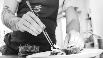 A person in a dark apron with a floral design, using chopsticks to eat from a white plate.