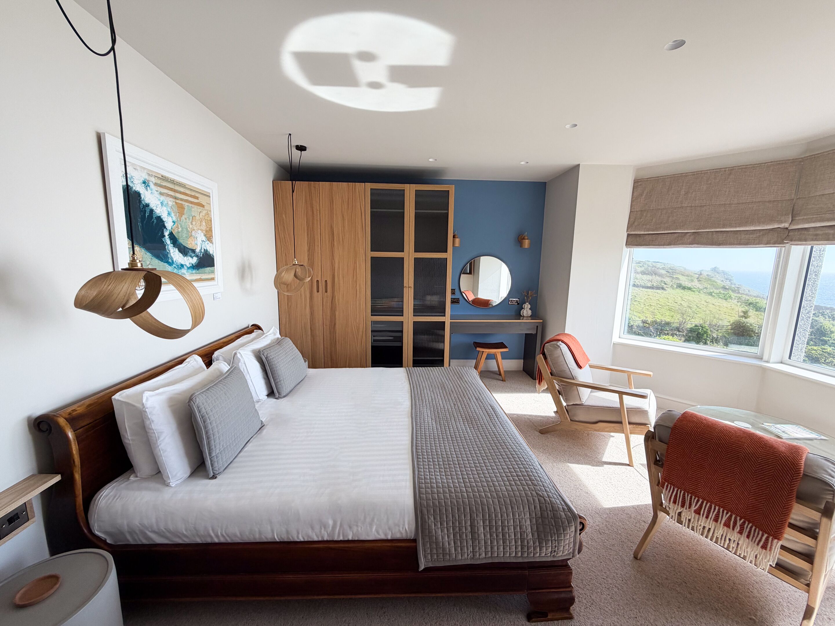 A bedroom with a bed, a wardrobe, a desk, a chair, a mirror, and a window with a view.