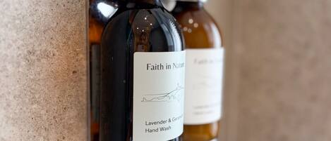 Two hand wash bottles mounted on a wall, one labeled 'Faith in Nature' with lavender and geranium scents.