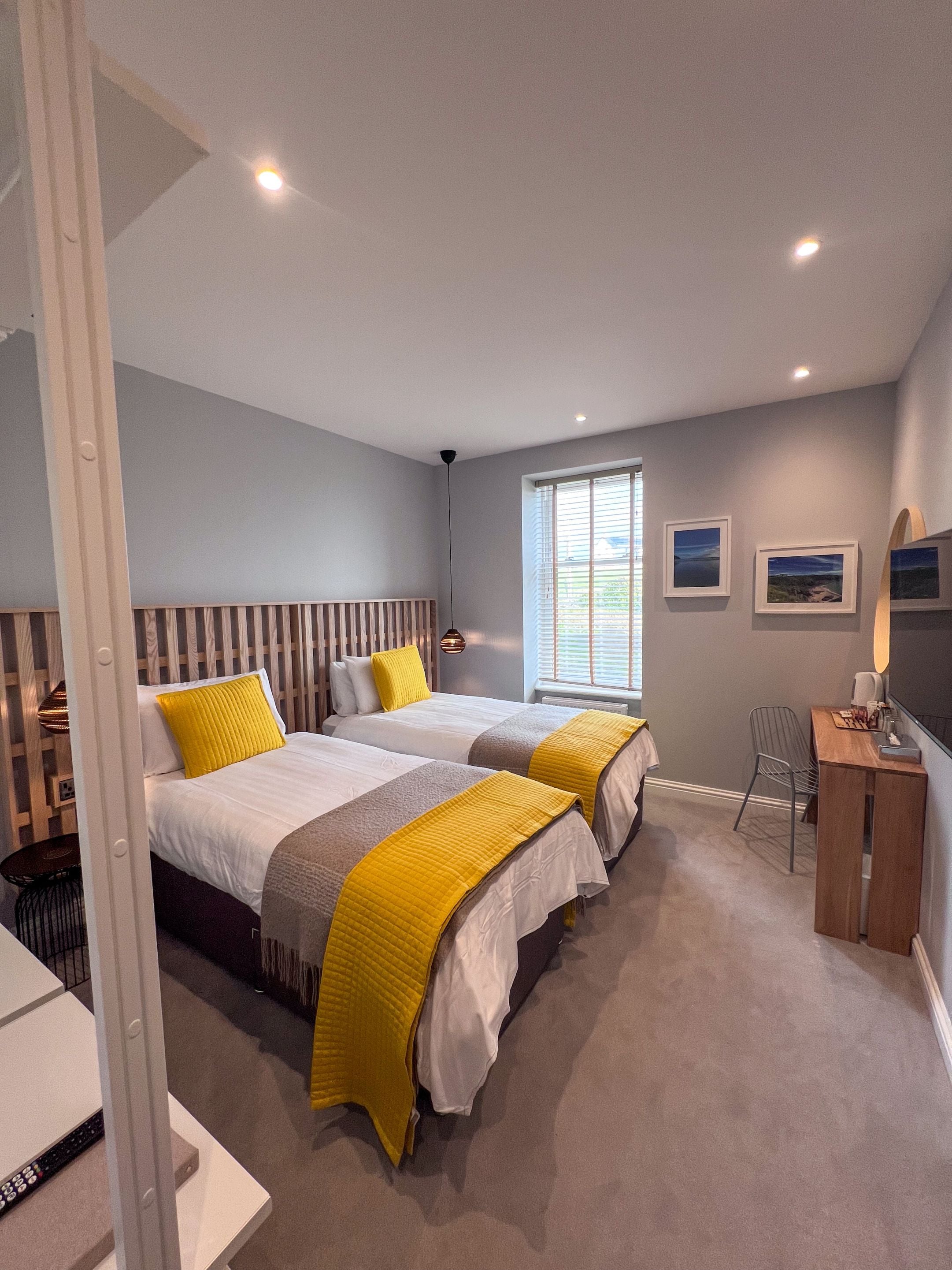 Een slaapkamer met twee bedden, een bureau en een raam met zonwering.