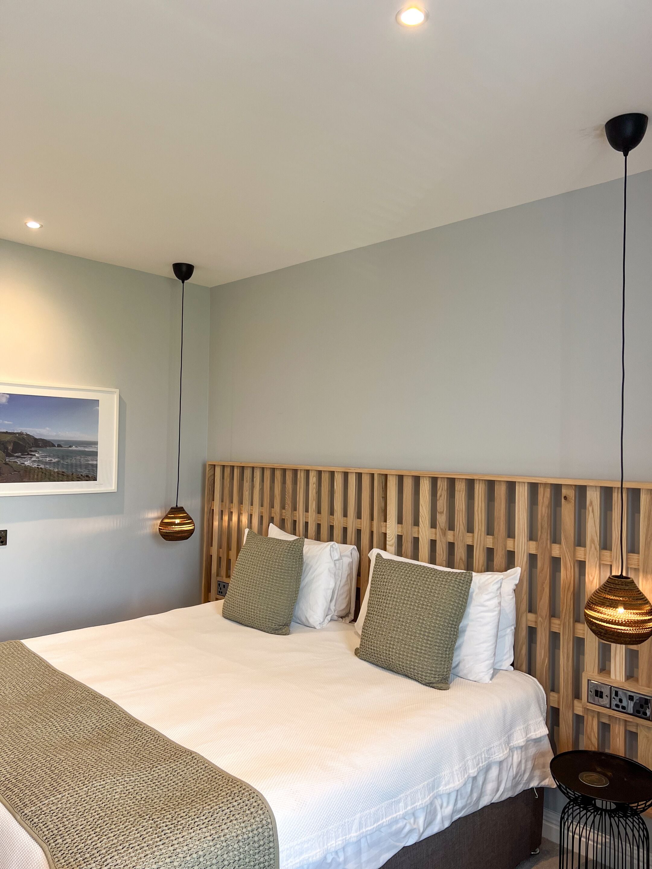 Un dormitorio moderno con una cama grande, cabecera de madera y dos lámparas colgantes.
