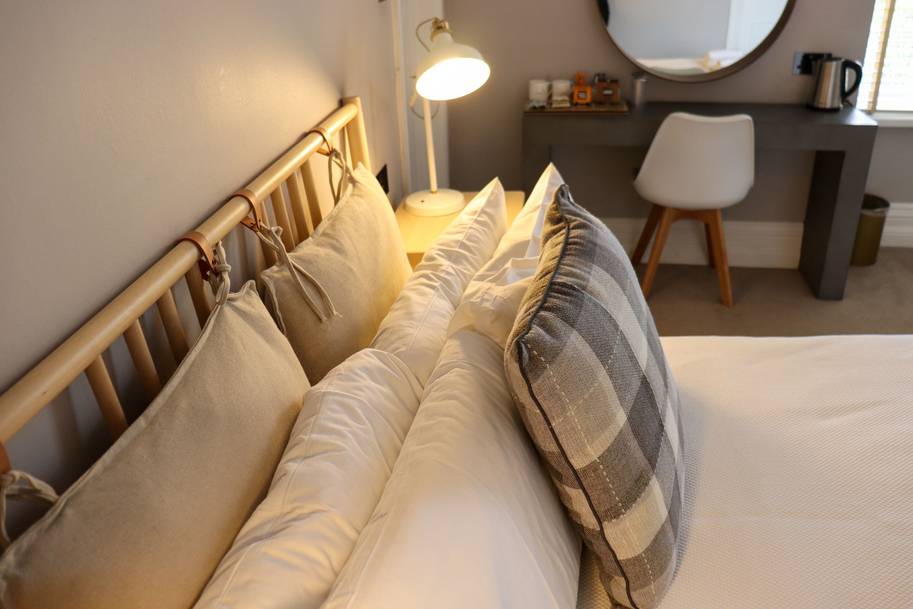 A neatly made bed with white and beige bedding, a wooden headboard, and a bedside lamp.