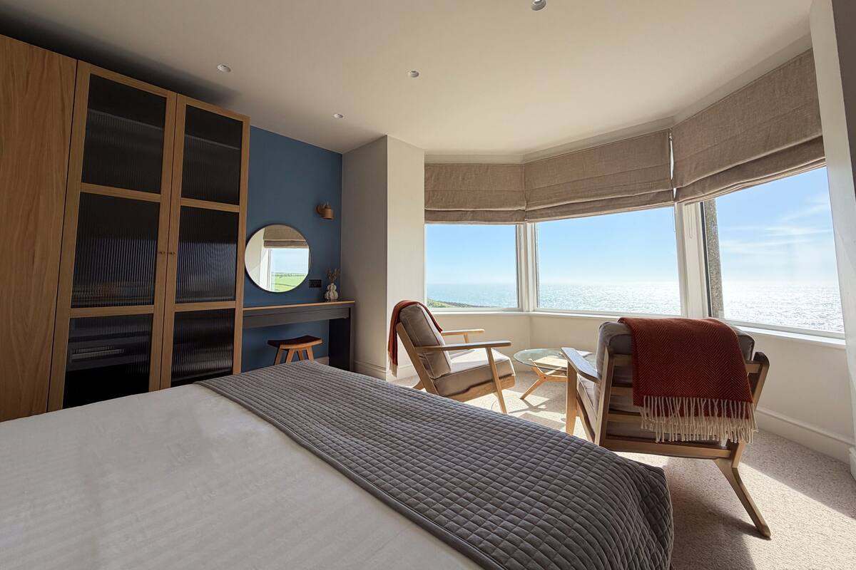 A bedroom with a bed, a desk, a chair, a wardrobe, and a large window with a view.