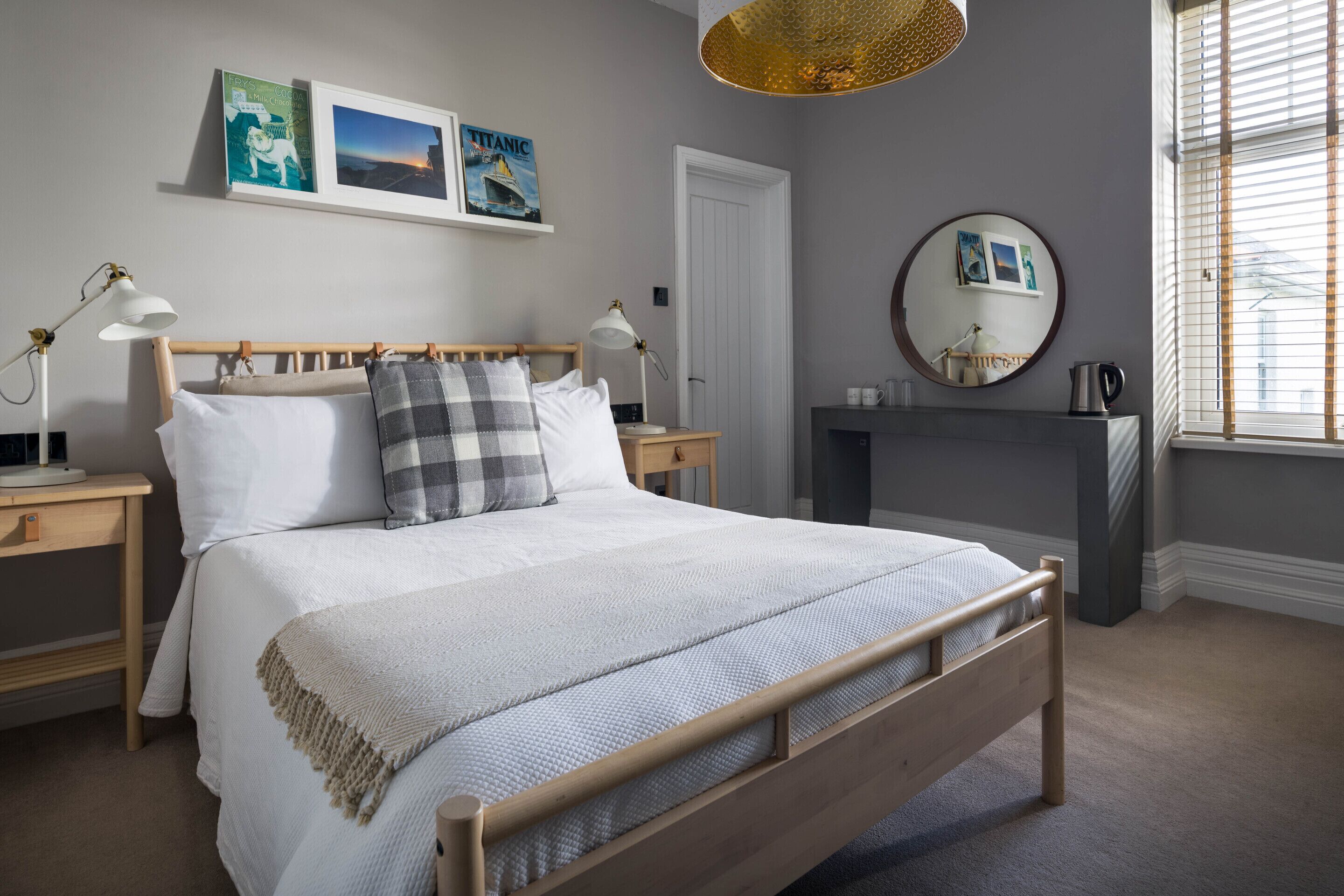 A neatly arranged bedroom with a wooden bed, bedside tables, a dresser, and a large window with blinds.
