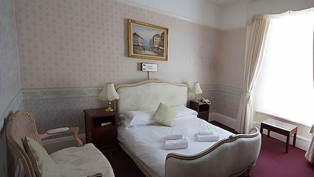 A hotel room with a large bed, two bedside tables, a chair, a nightstand, a painting on the wall, and a window with curtains.