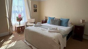A neatly arranged hotel room with a large bed, a bedside table, a chair, and a window with curtains.