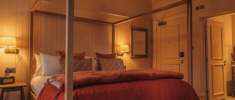 A four-poster bed with a red bedspread, a wooden floor, and a ceiling light fixture.