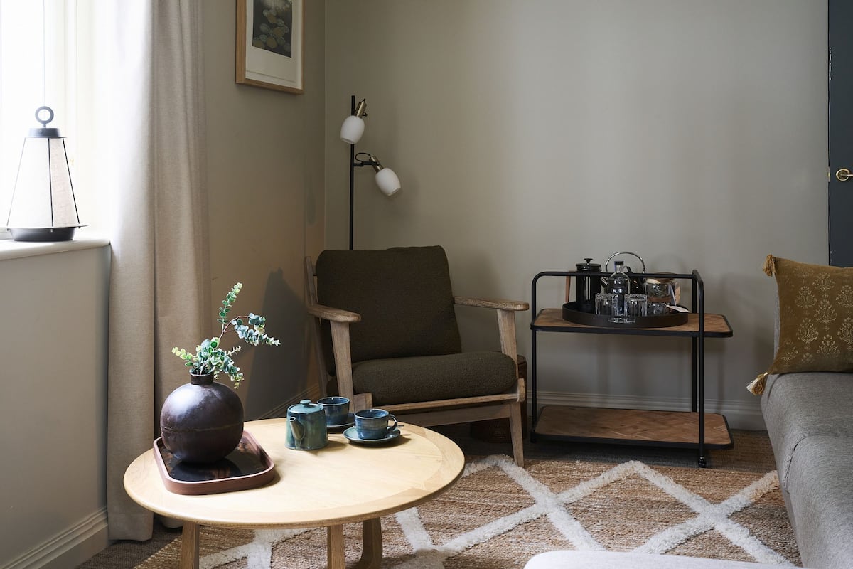 A cozy living room with a round wooden table, a chair, a sofa, a floor lamp, and a small side table with a tray.