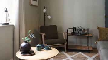 A cozy living room with a round wooden table, a chair, a sofa, a floor lamp, and a small side table with a tray.