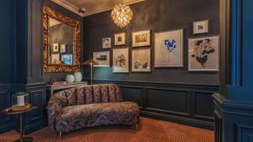 Una habitación con una pared oscura, un espejo grande y ornamentado, un sofá estampado y un suelo con estampado de espiga.