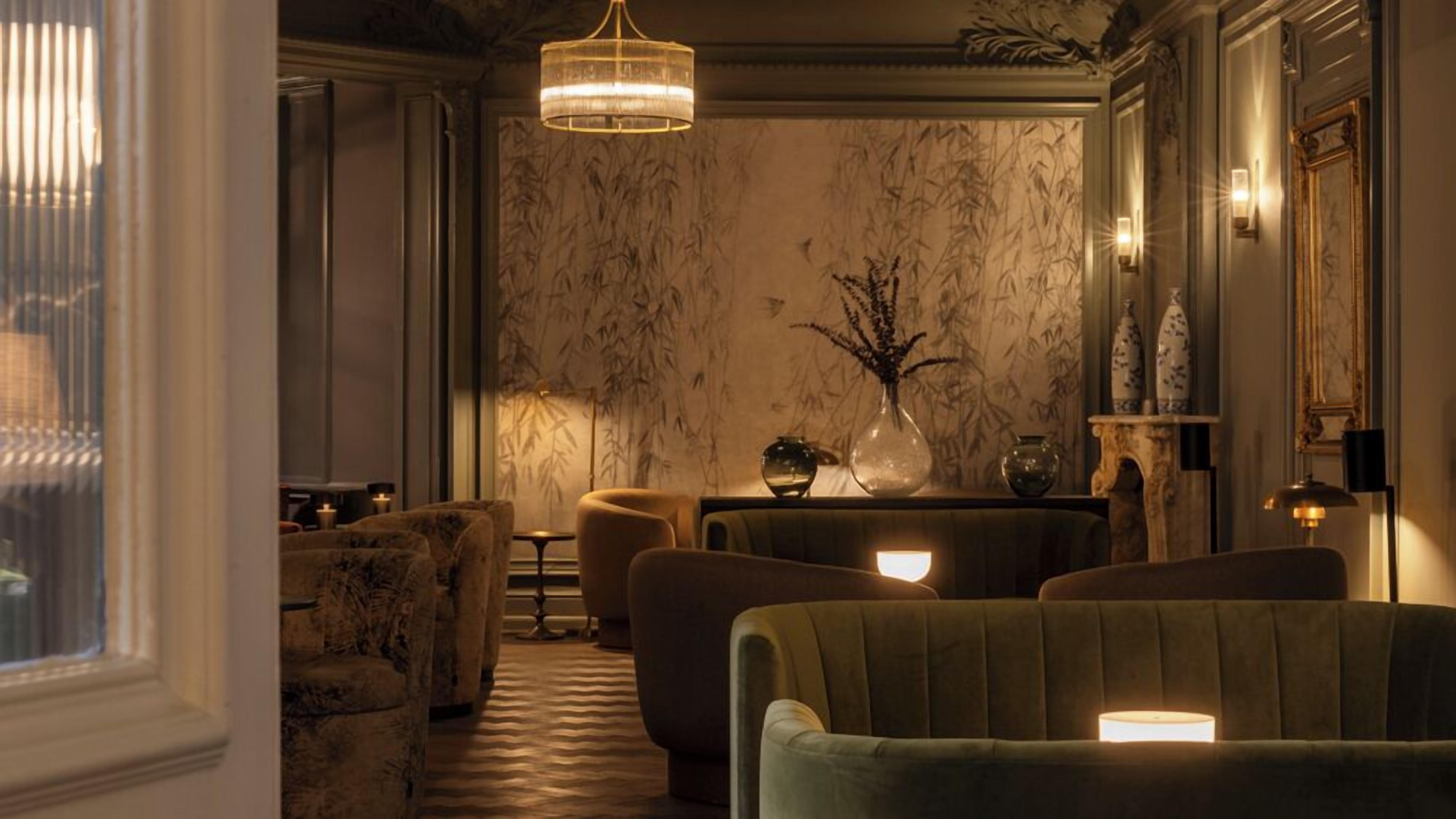 A room with a patterned wallpaper, a chandelier, a vase with branches, and a sofa.