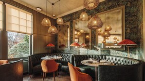 Un restaurante con asientos tipo banca de cuero negro, mesas redondas y lámparas colgantes de fibra.