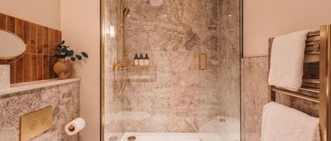 A modern bathroom with a glass-enclosed shower, marble walls, a gold-framed mirror, and a towel rack.