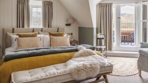 Un dormitorio con una cama grande, un banco de madera, una mesita pequeña y vistas al exterior a través de un ventanal.
