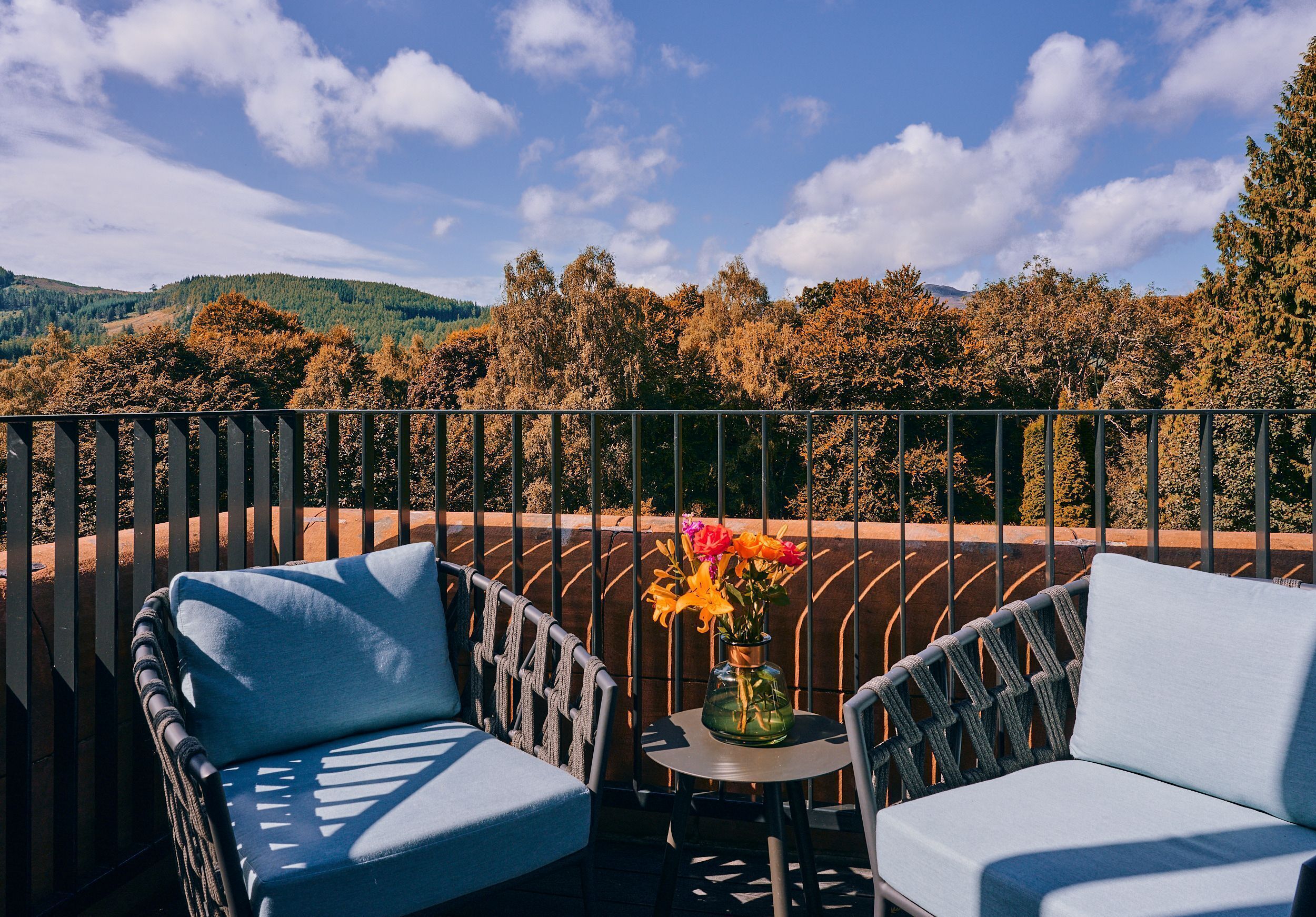A balcony with two chairs, a small table, and a vase of flowers.