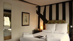 Ein Hotelzimmer mit einem großen Bett, einem Nachttisch mit Lampe, einem gerahmten Pflanzenbild an der Wand und einem Spiegel, der einen Teil des Zimmers reflektiert.