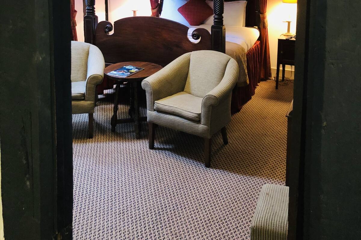 A bedroom with a four-poster bed, a chair, a small table, and a lamp.
