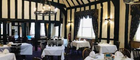 A traditional inn with exposed wooden beams and white walls. Tables are set with white tablecloths and silverware.