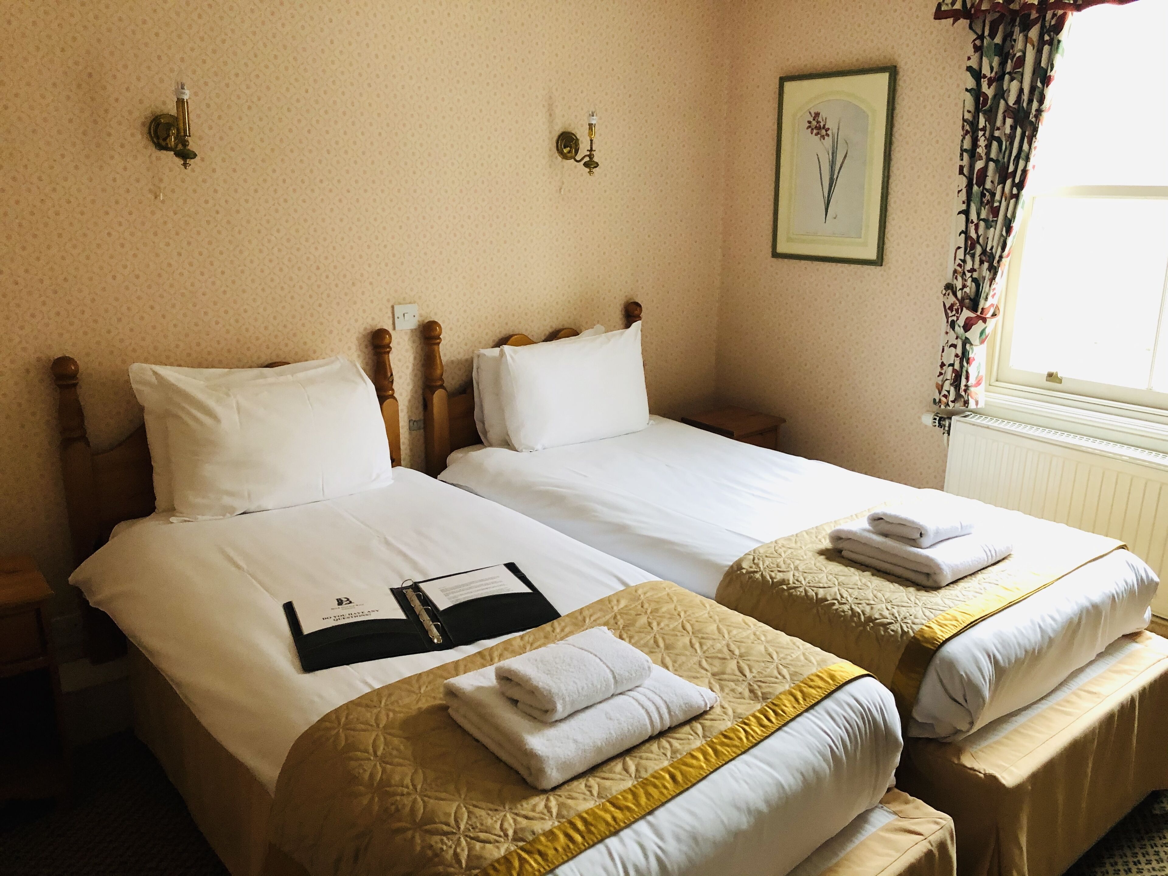 Habitación de hotel con dos camas individuales, una mesita de noche, un cuadro enmarcado en la pared y una ventana con cortinas.