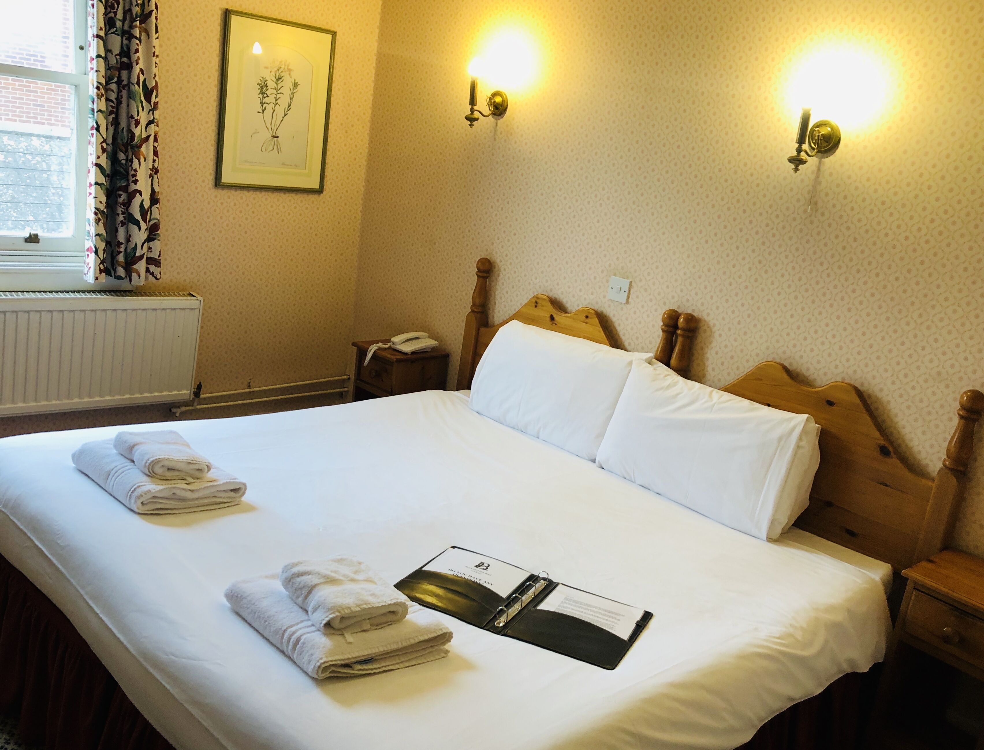 A neatly made bed with white linens, a bedside table with a lamp, and a framed picture on the wall.
