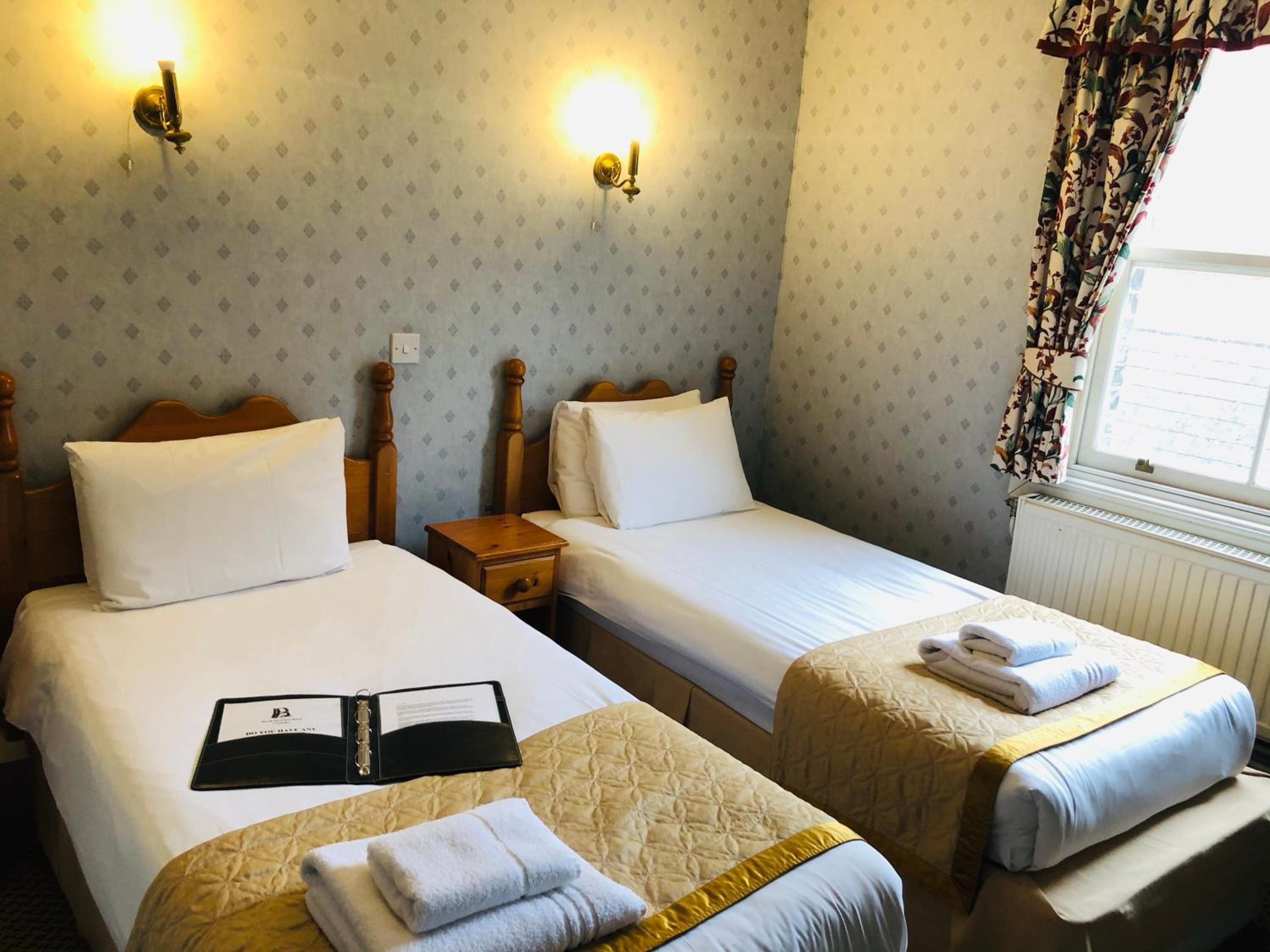 A hotel room with two beds, a nightstand, and a window with curtains.