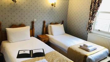 A hotel room with two beds, a nightstand, and a window with curtains.
