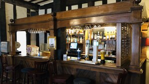 Eine Bar mit Holzbalken, Barhocker, einer Kasse und einer Auswahl an Flaschen und Gläsern.