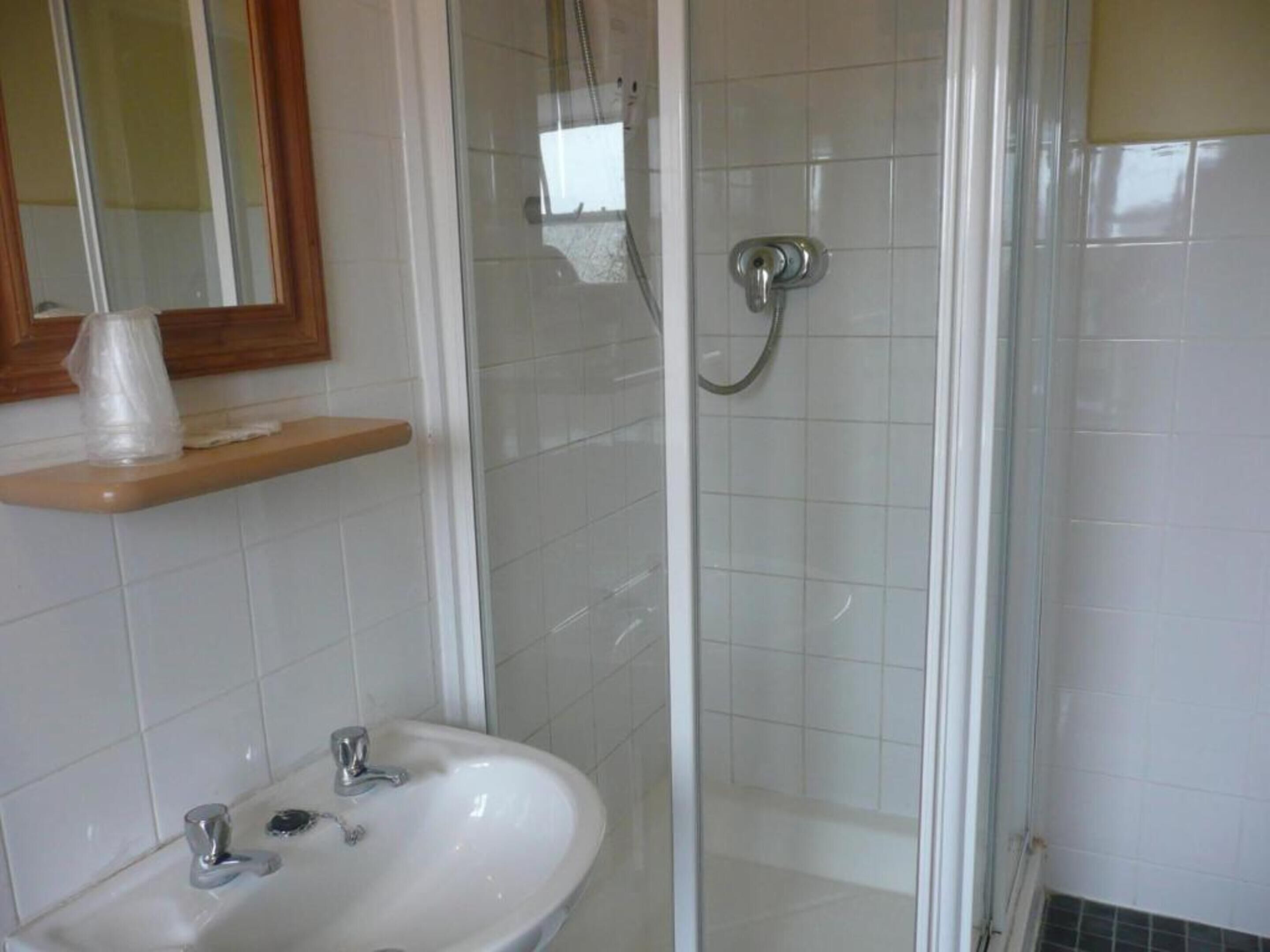 A bathroom with a glass-enclosed shower, a sink with two faucets, and a mirror above the sink.