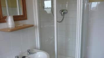 A bathroom with a glass-enclosed shower, a sink with two faucets, and a mirror above the sink.