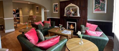 A spacious living room with green leather sofas, a wooden coffee table, and a fireplace.
