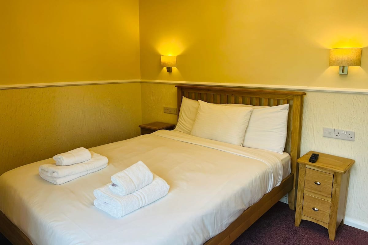 A hotel room with a bed, two bedside tables, and two wall-mounted lamps.