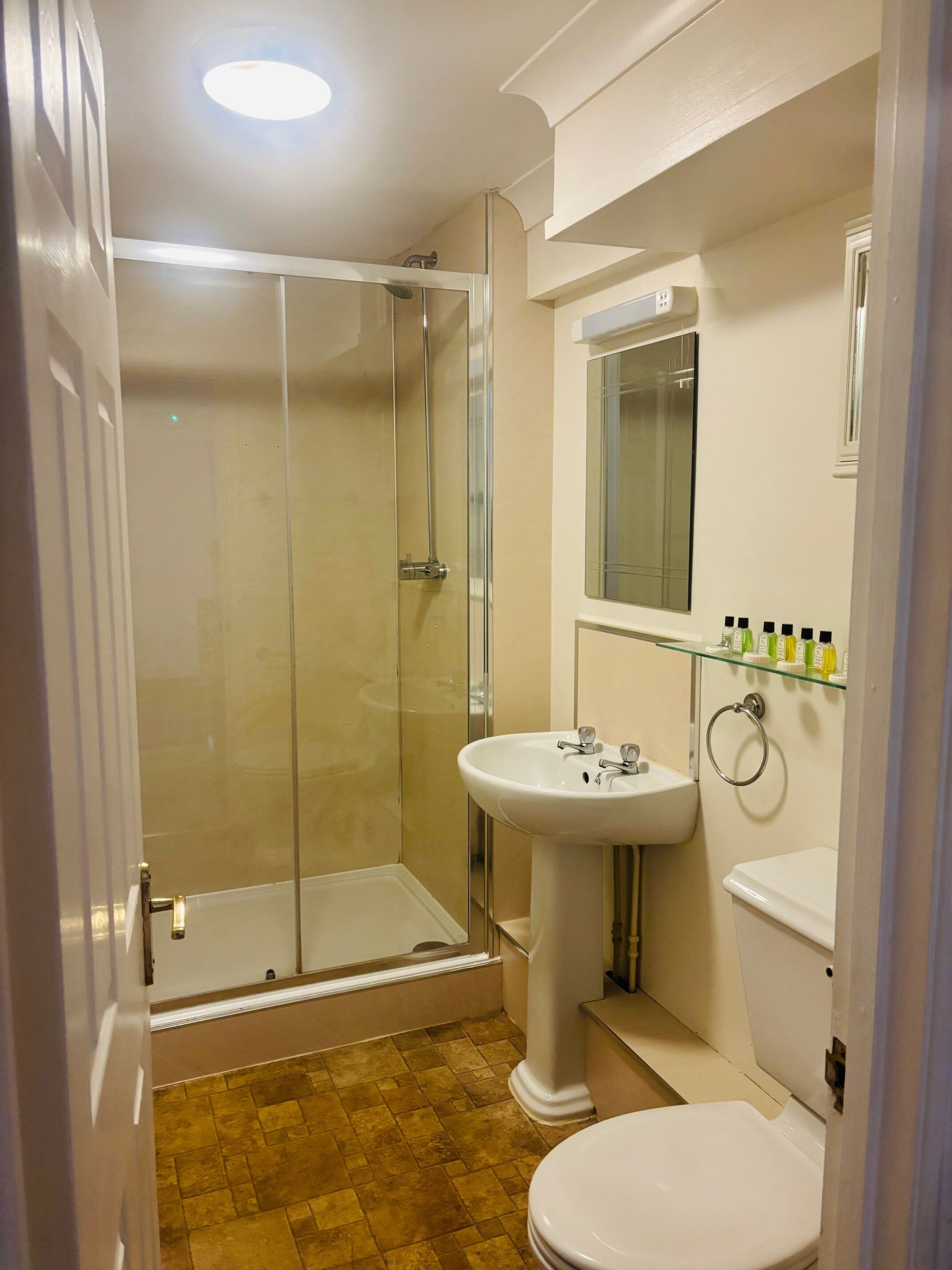 A bathroom with a glass shower enclosure, a pedestal sink, and a toilet.