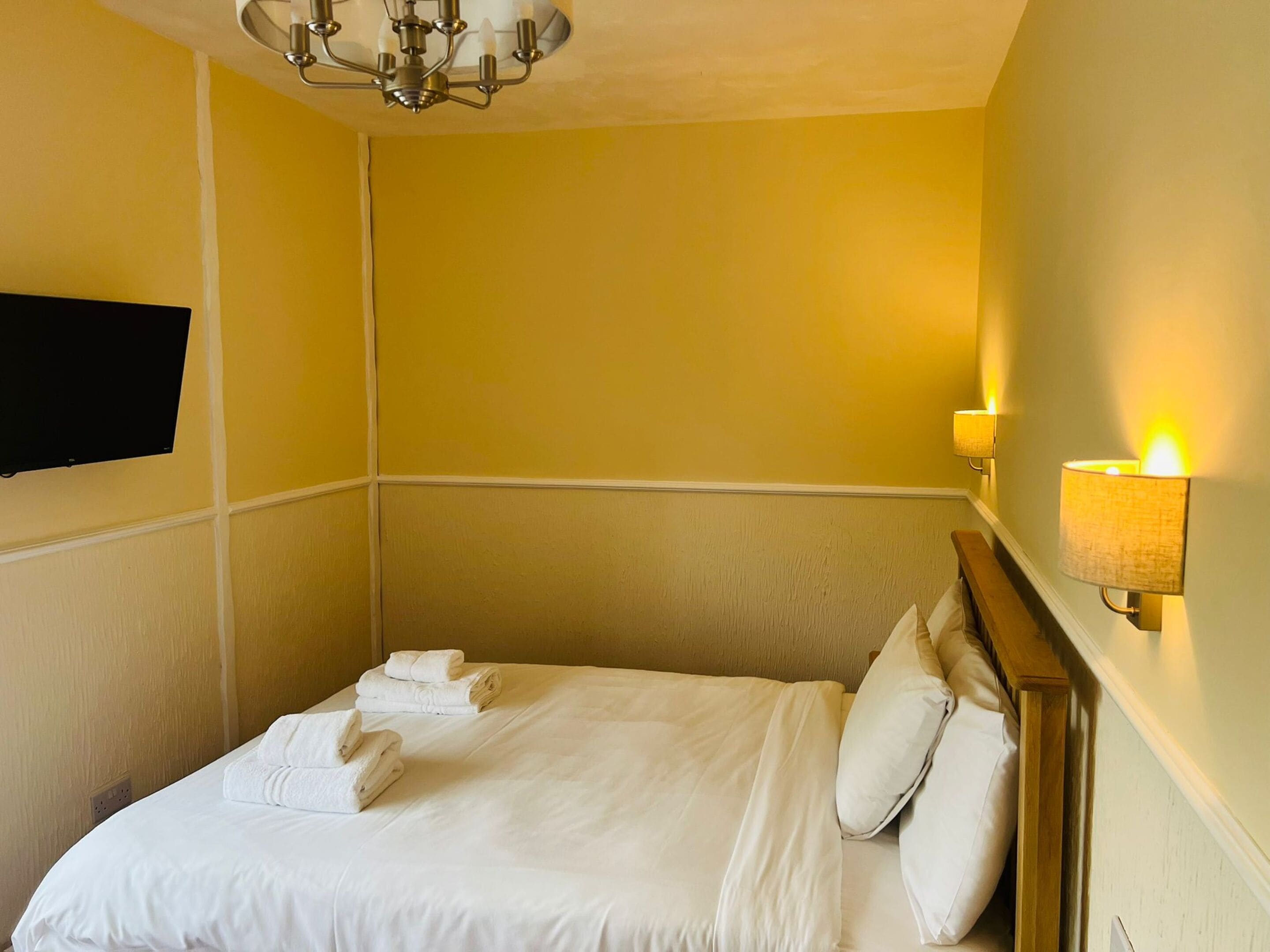 A hotel room with a bed, a chandelier, and wall-mounted lamps.