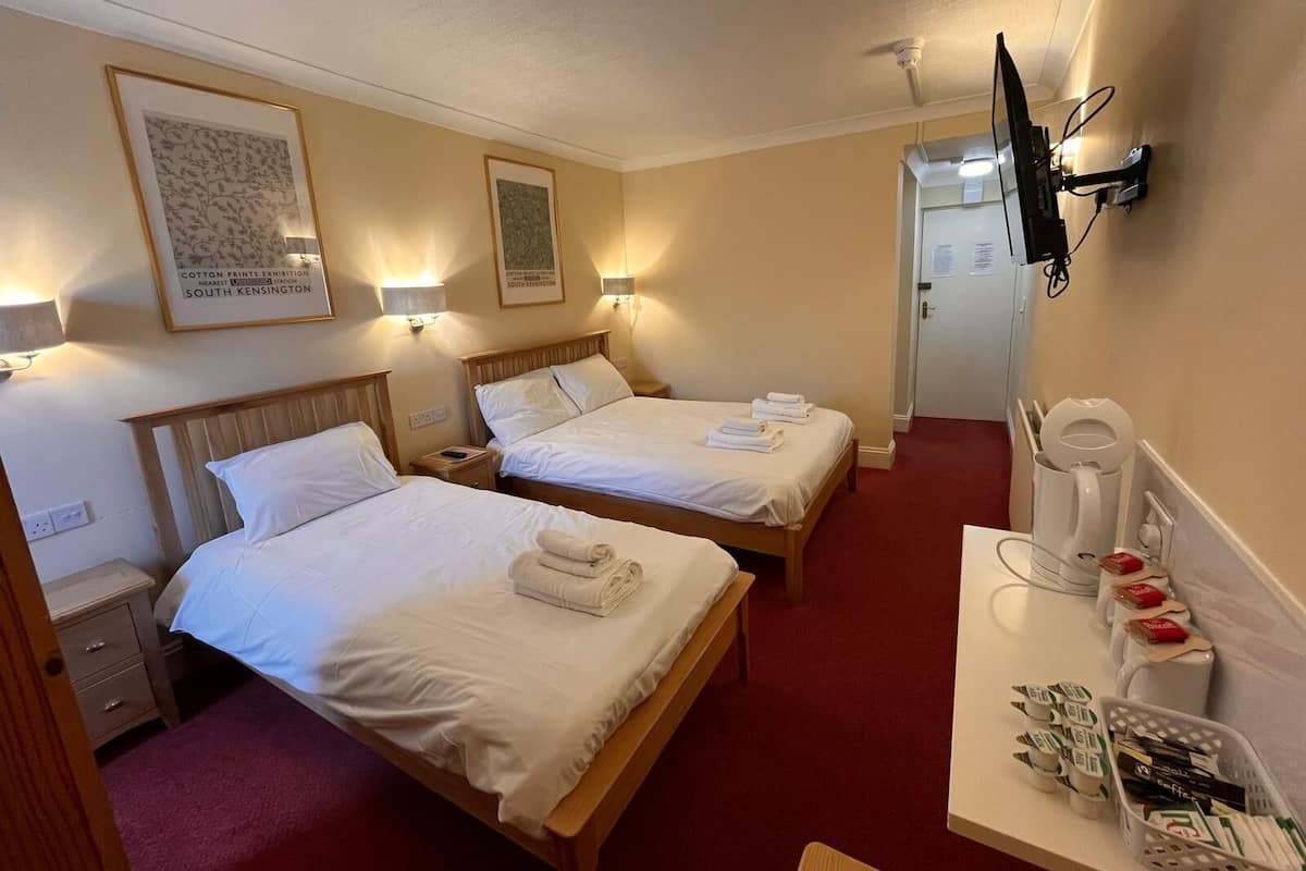 A hotel room with two beds, a desk with a coffee maker, and a TV mounted on the wall.