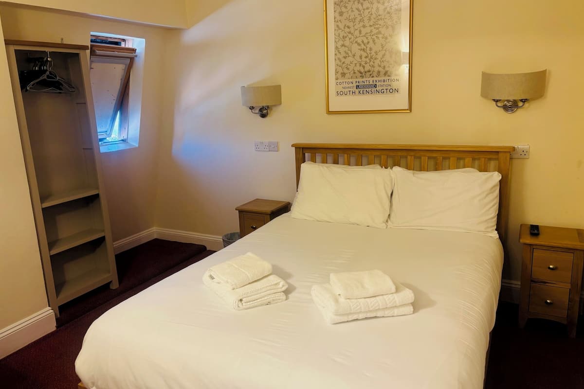 A hotel room with a neatly made bed, a wardrobe, two bedside lamps, and a framed picture on the wall.