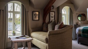 A cozy room with a sofa, a small table, and a bed. There are large windows with curtains, a mirror on the wall, and framed pictures. - Red Lion Hotel and Manor House (Skipton)