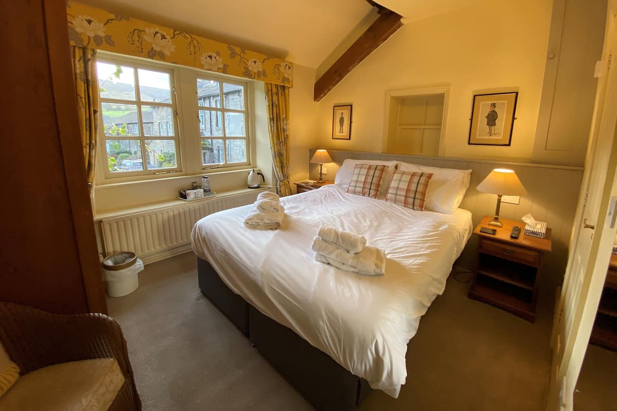 A hotel room with a large bed, two bedside tables, a window with curtains, a radiator, and a view of the outside.