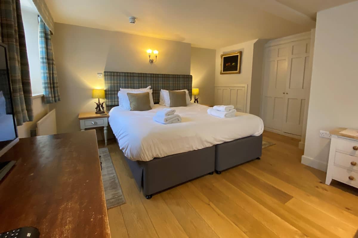 A hotel room with a large bed, bedside lamps, a headboard, a nightstand, a desk, and a wardrobe.