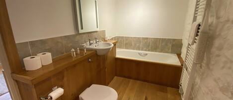 Un baño con tocador de madera, lavamanos, inodoro y bañera.