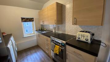 A compact kitchen with wooden cabinets, a black countertop, a stove, and a toaster.