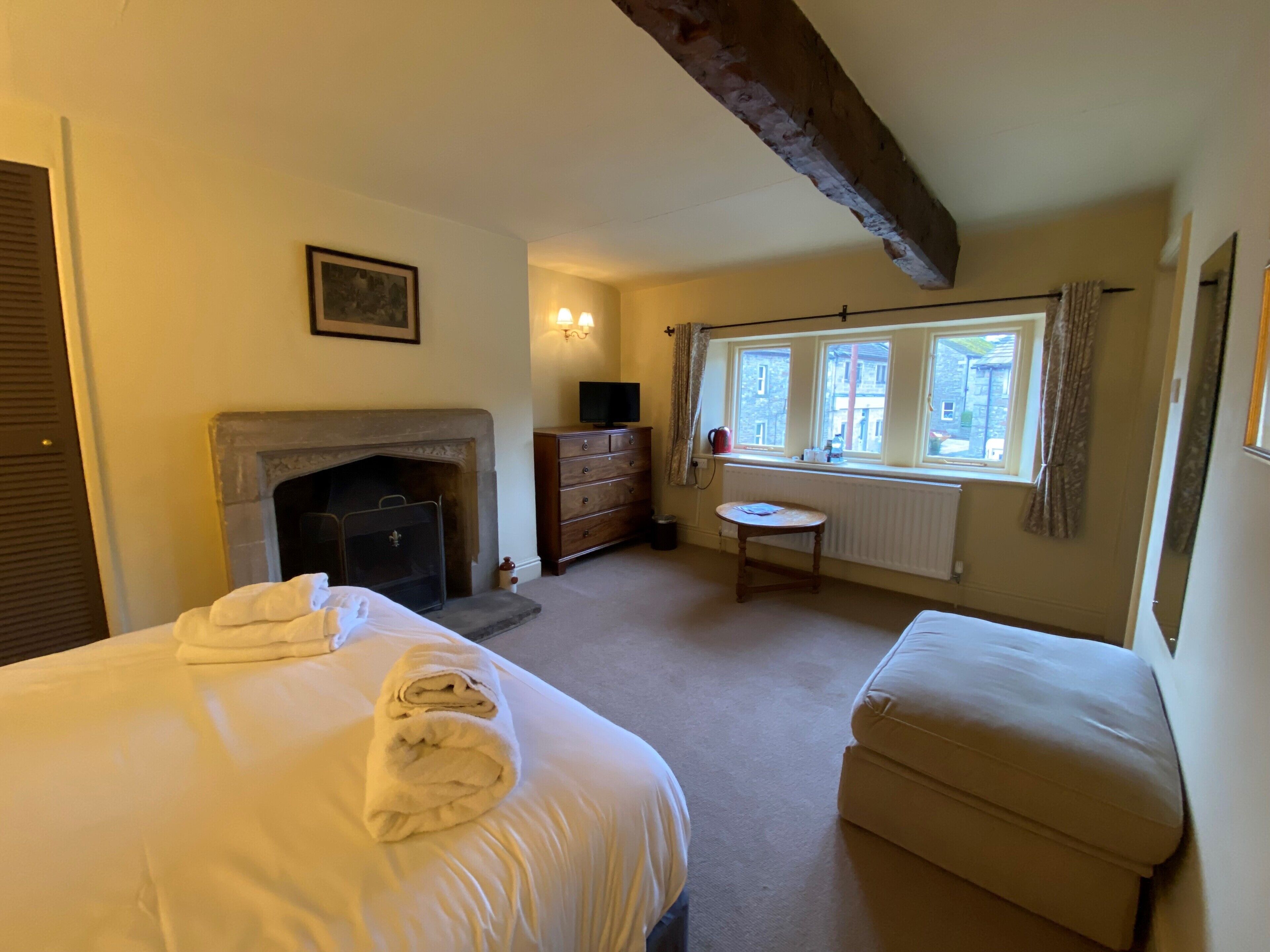 A bedroom with a bed, a dresser, a small table, a radiator, and a window with curtains.